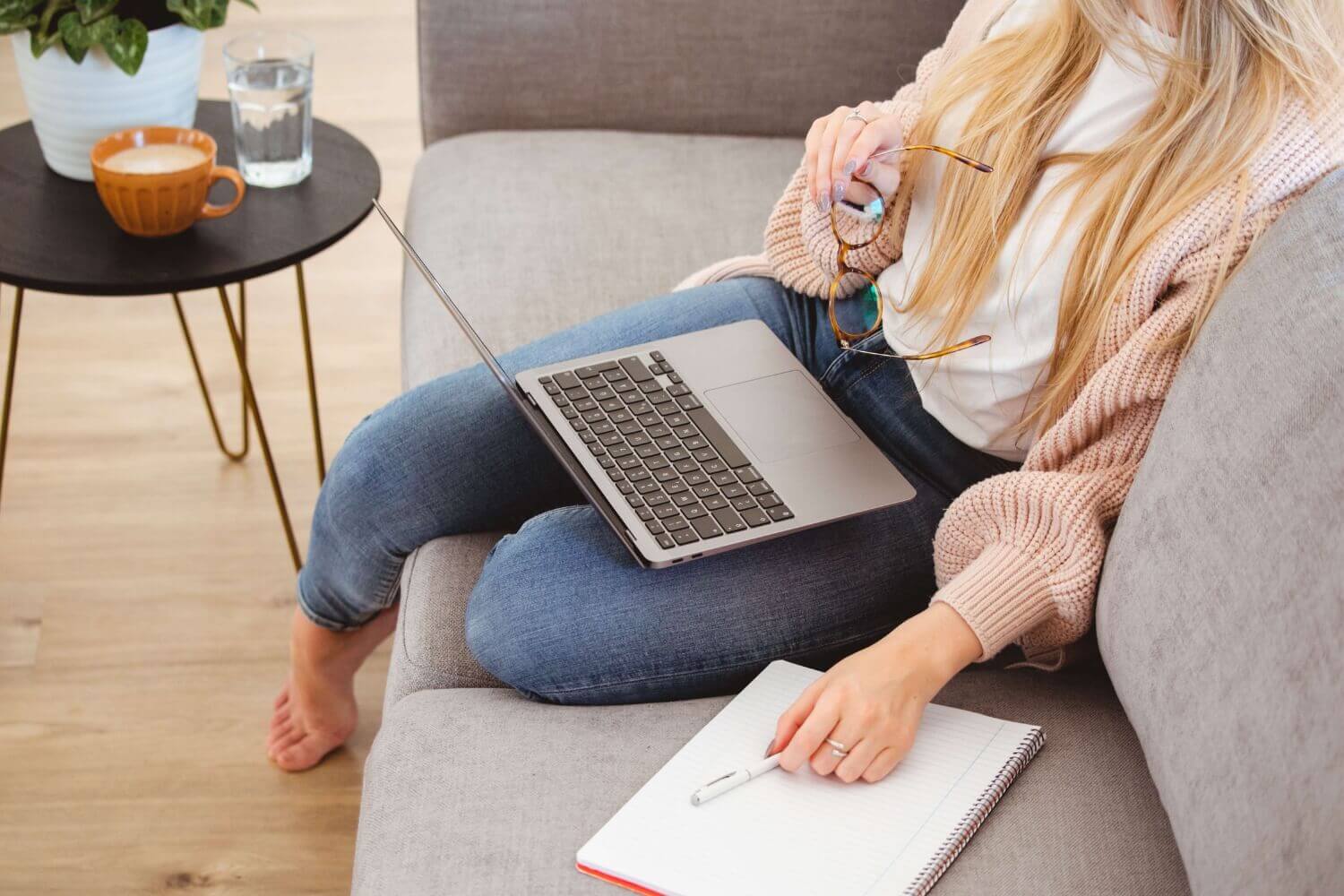 Freelancer working from home on a laptop with notebook and coffee on sofa
