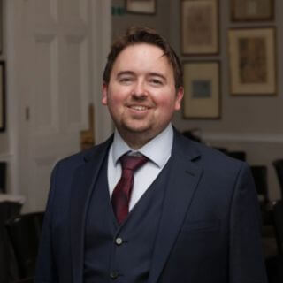 Dr Iain Campbell, Lead Director and Head of AI Policy, Ethics & Transformation at HLA Scotland, commentator on IR35 status. Blue suit & red tie, smiling